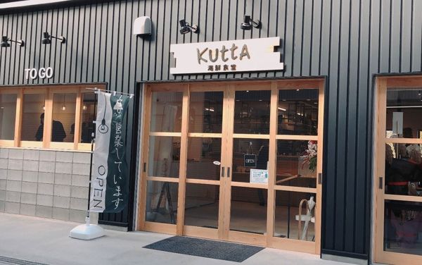 KUTTAの入口。グレーの外壁に木の扉と「KUTTA 海鮮食堂」の看板